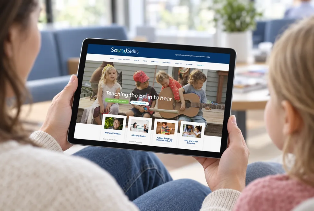 A parent holding a tablet showing the SoundSkills website home page in a clinic waiting room